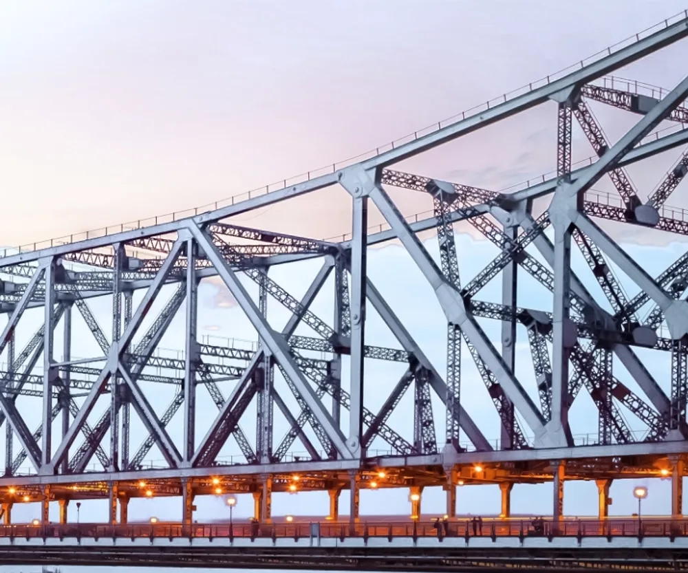 The steel trusswork of the Howrah Bridge against an evening sky.