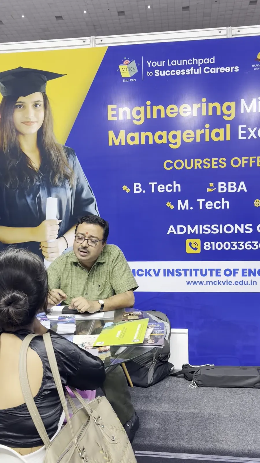 A visitor seated in consultation at a stall advertising engineering and management courses.