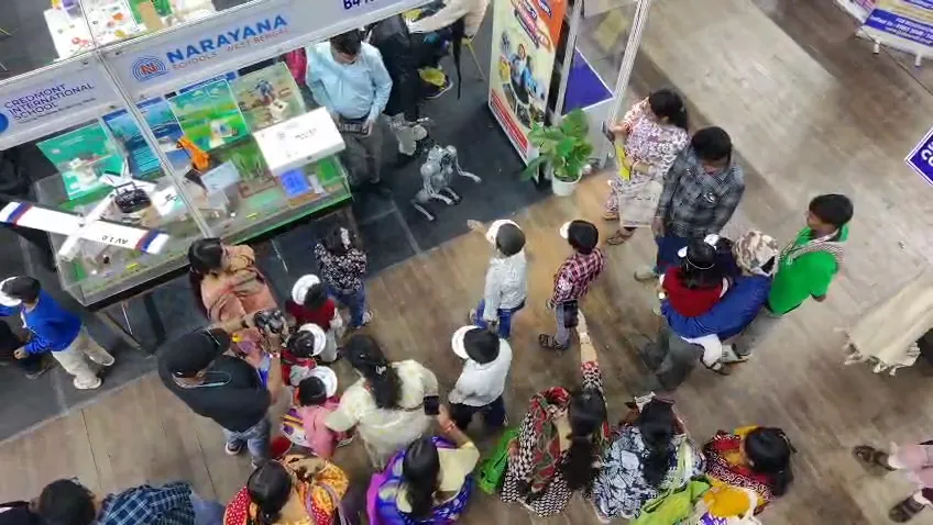 Crowd of visitors filling an aisle between exhibition stalls, seen from above.