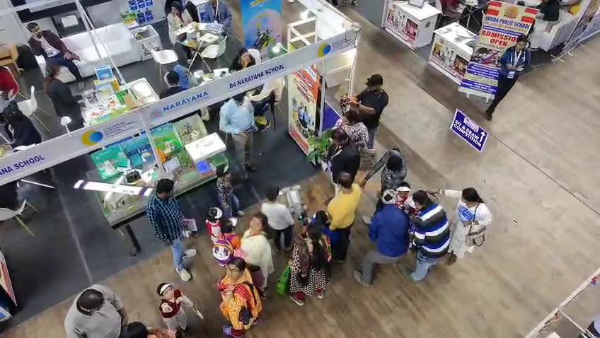 Visitors walking along a busy aisle lined with school stalls.