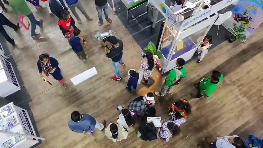 Visitors in conversation at stall counters across the exhibition floor.