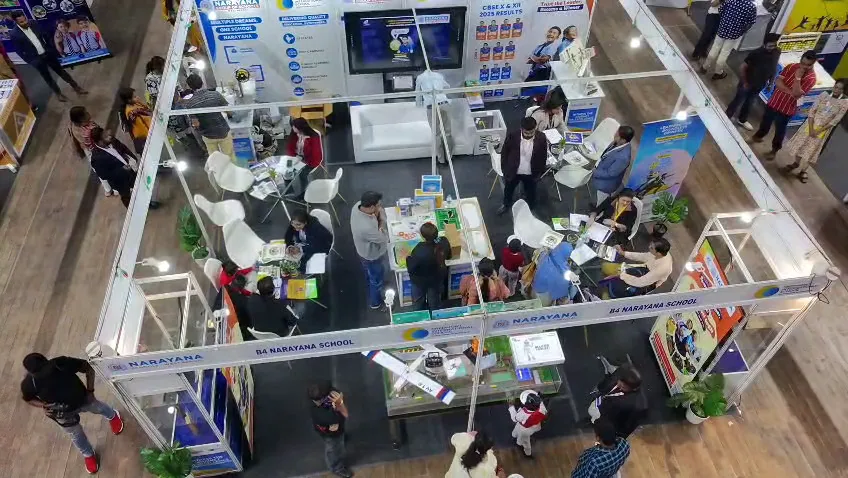 Elevated view across rows of exhibition stalls with visitors moving between them.