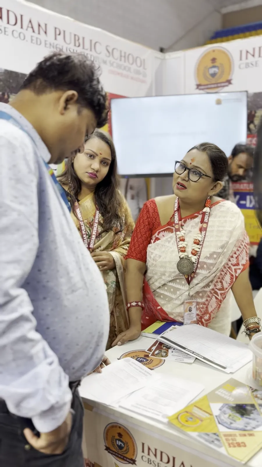 Two visitors talking with a representative across a school stall counter.