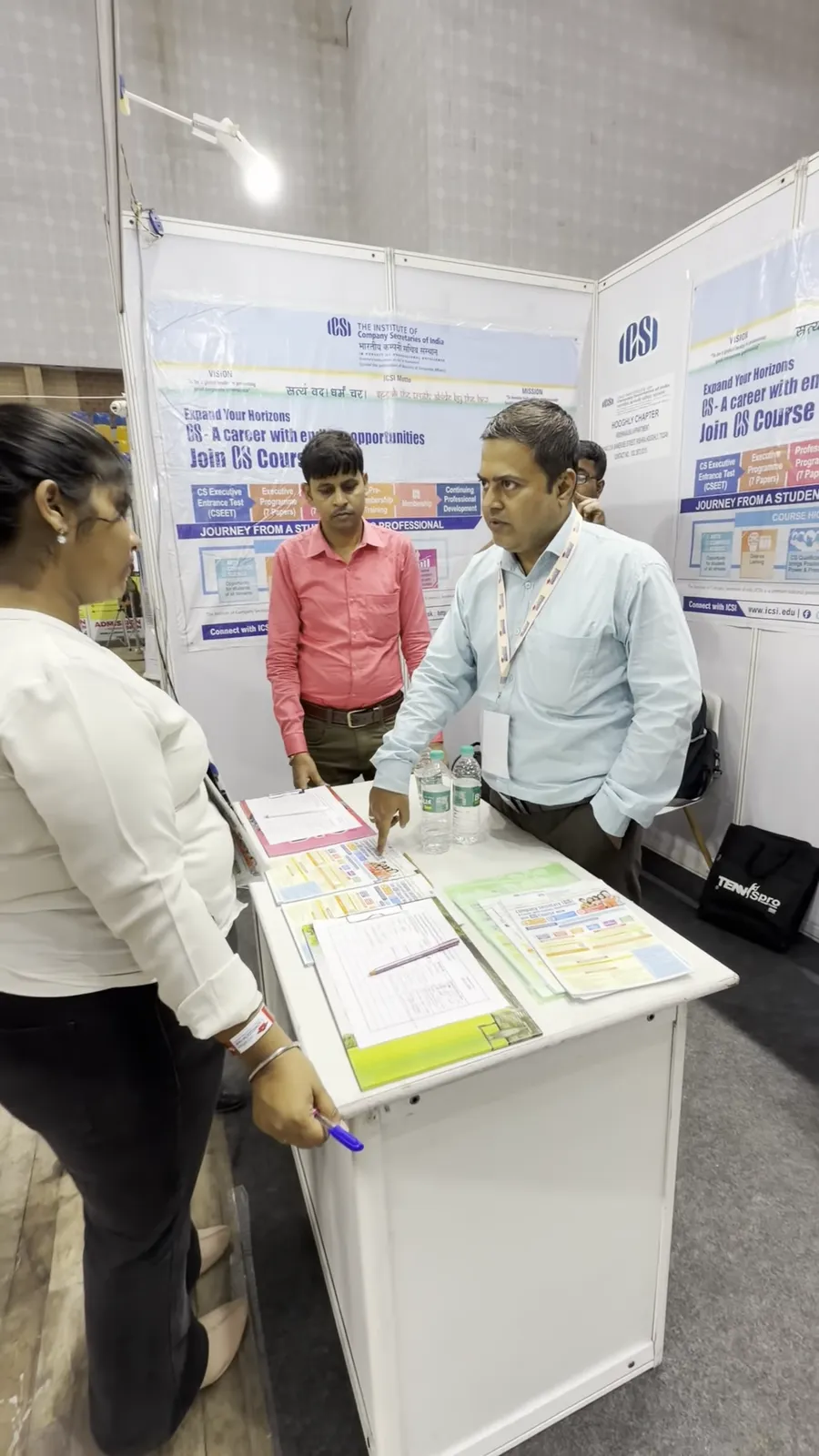 A group of visitors talking with a representative at a stall counter.