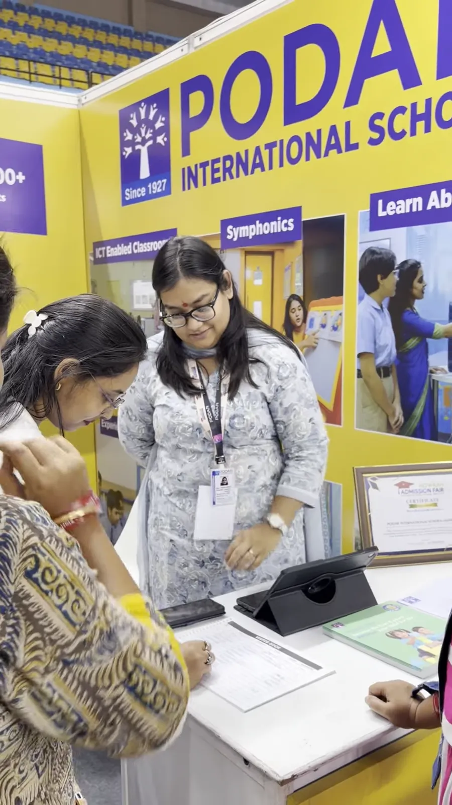 A visitor filling in a form at the Podar International School stall counter.