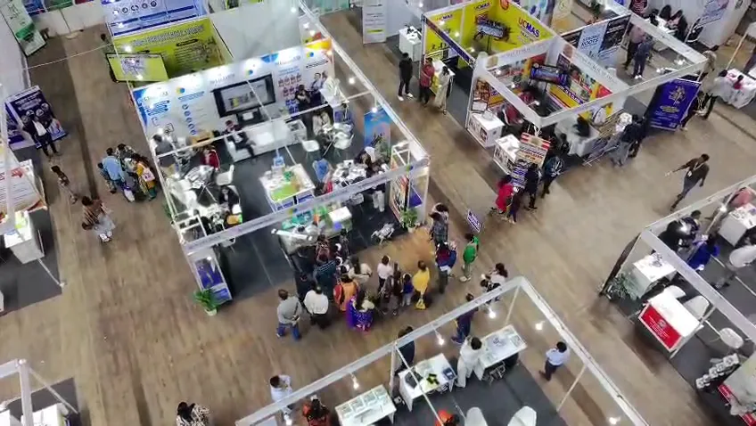 Grid of exhibition stalls seen from above with visitors walking between them.