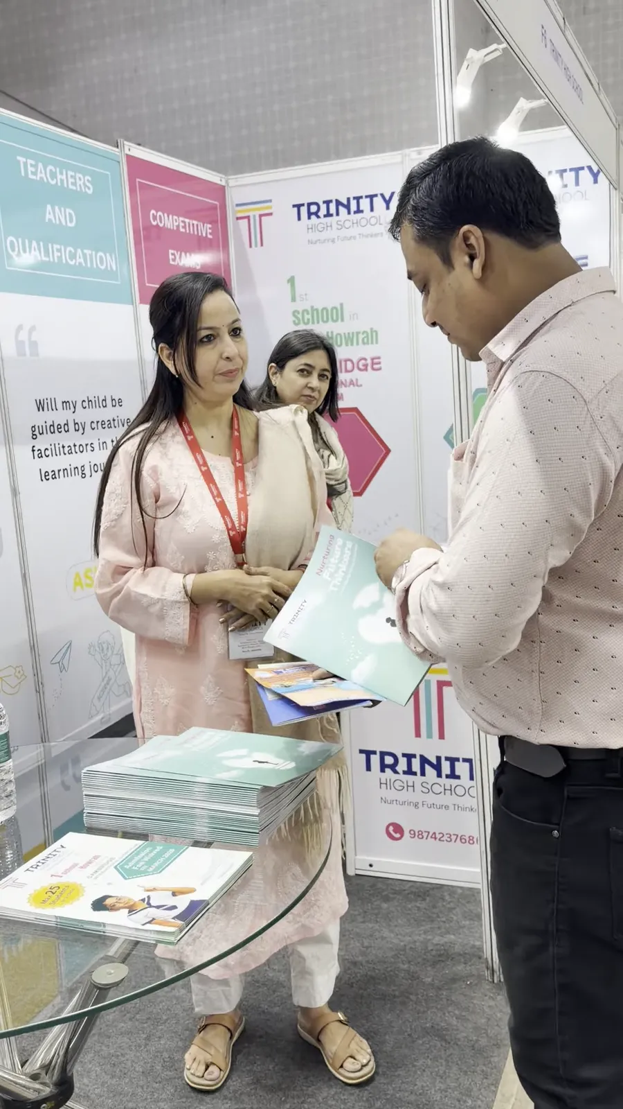 A representative handing printed material to a visitor at the Trinity stall.